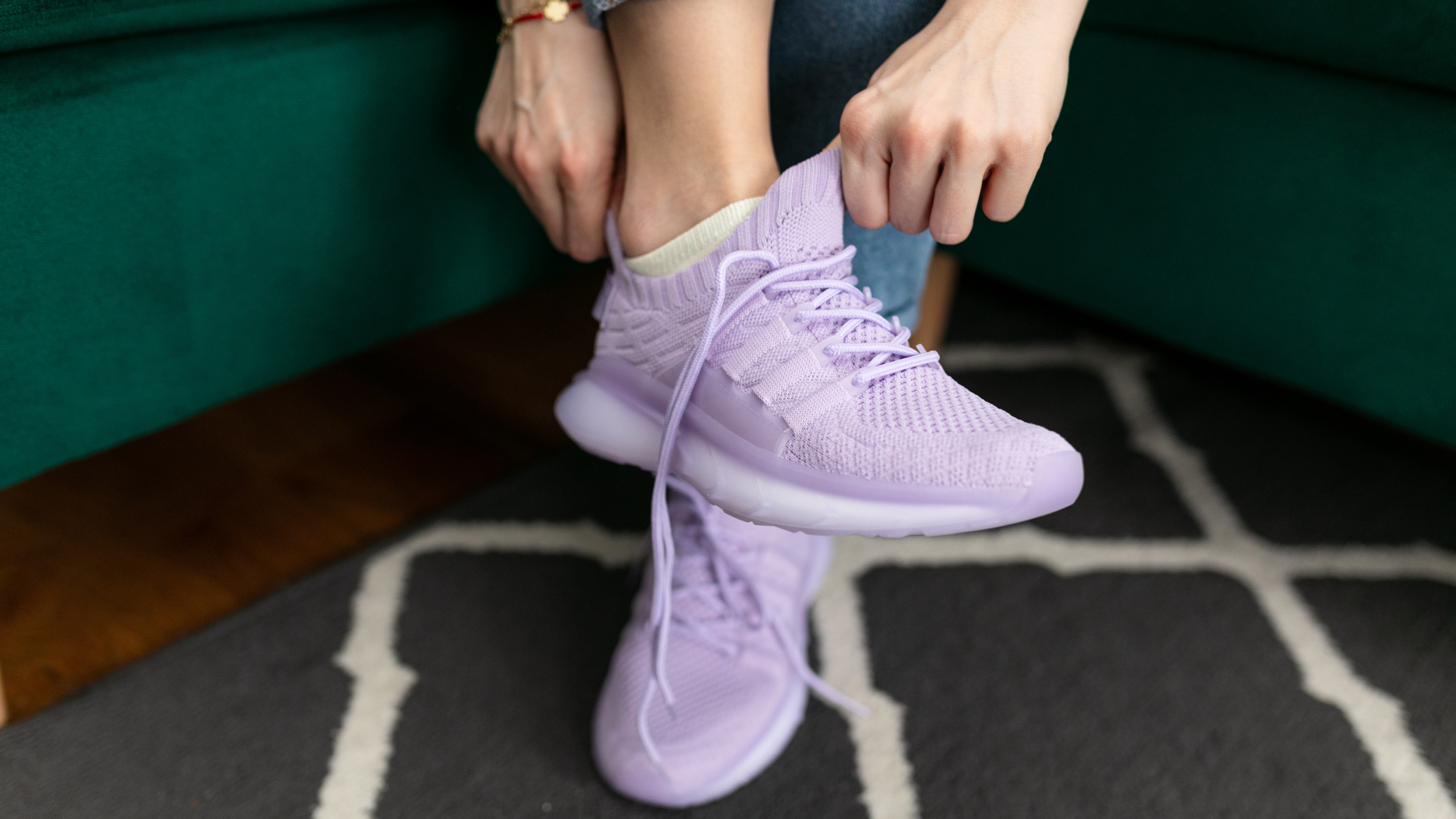 Unrecognizable cropped female hands trying on sportive pink sneakers, trying on and testing footwear, sitting in green armchair. Big size for women, orthopedic shoe, bodycare. Low angle view, flooring