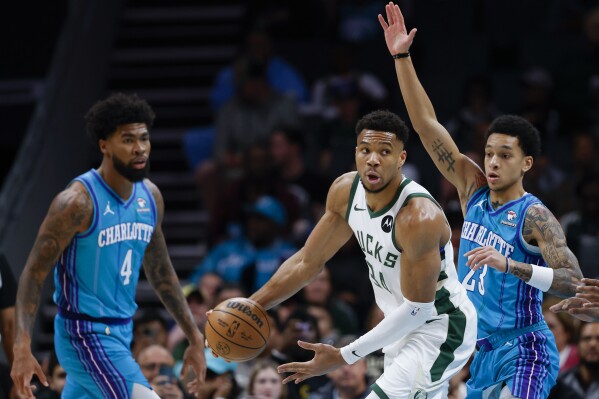 Milwaukee Bucks forward Giannis Antetokounmpo, center, looks to pass against Charlotte Hornets guard Tre Mann, right, as Hornets center Nick Richards (4) looks on during the first half of an NBA basketball game in Charlotte, N.C., Thursday, Feb. 29, 2024. (AP Photo/Nell Redmond)