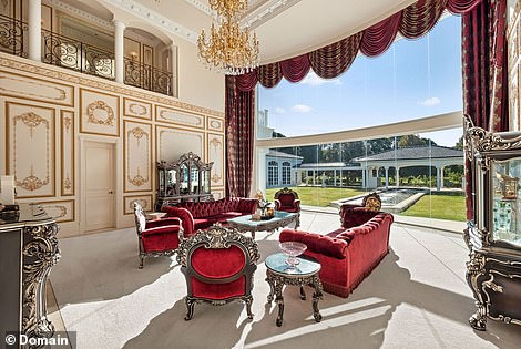 Another over-sized chandelier hangs from the double-height ceiling over a glamorous formal lounge room with a fireplace and dramatic two-storey window that lets sunlight pour in during the day